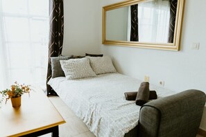 Un dormitorio ordenado con cama, almohadas, una silla, una mesa y un espejo.