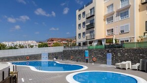 A pool area with two circular pools, a stone wall, and a view of buildings in the background. - Spacious 2 Bedroom Golden Apartment (Callao Salvaje)