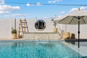 A swimming pool with a white textured wall, a hexagonal window, a wooden ladder, potted plants, and a beige umbrella. - NEW Heated Pool King bed Tulum inspired Home (Scottsdale)