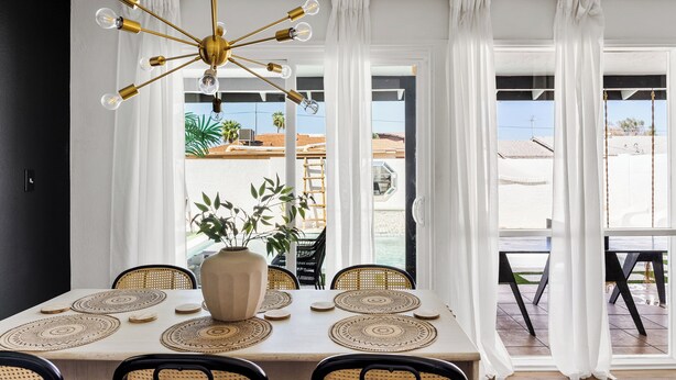 Un coin repas avec une table dressée pour quatre personnes, un vase décoratif et un lustre moderne.