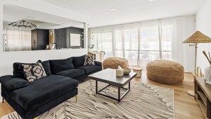 Un salon moderne avec un canapé foncé, une table basse et une grande fenêtre ornée de rideaux légers.