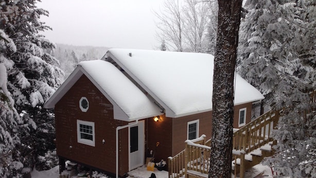 Een besneeuwde houten chalet met een voordeur, een trap en een klein veranda.