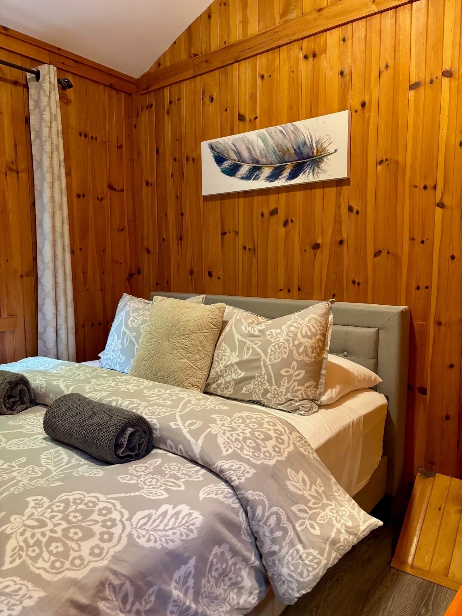 A wooden-paneled room with a bed, a feather artwork on the wall, and a curtain.