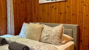 Een kamer met houten lambrisering, een bed en een gordijn, met een kunstwerk van veren aan de muur.