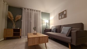 A living room with a sofa, a wooden coffee table, a floor lamp, a side table with a vase, and a curtain.