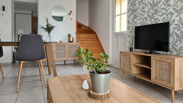 A modern living room with a wooden dining table, a TV on a wooden stand, a staircase, and a floral wallpaper.