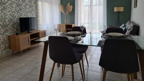 A dining area with a glass table, black chairs, and a wooden sideboard with a television.