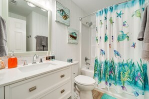 Un baño con un lavamanos blanco, dos espejos, un inodoro y una cortina de ducha con motivos marinos.