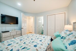 Un dormitorio con cama, televisor, cómoda y puerta que da a otra habitación.