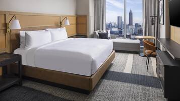 A hotel room with a large bed, a desk, a chair, a TV, and a view of a cityscape.