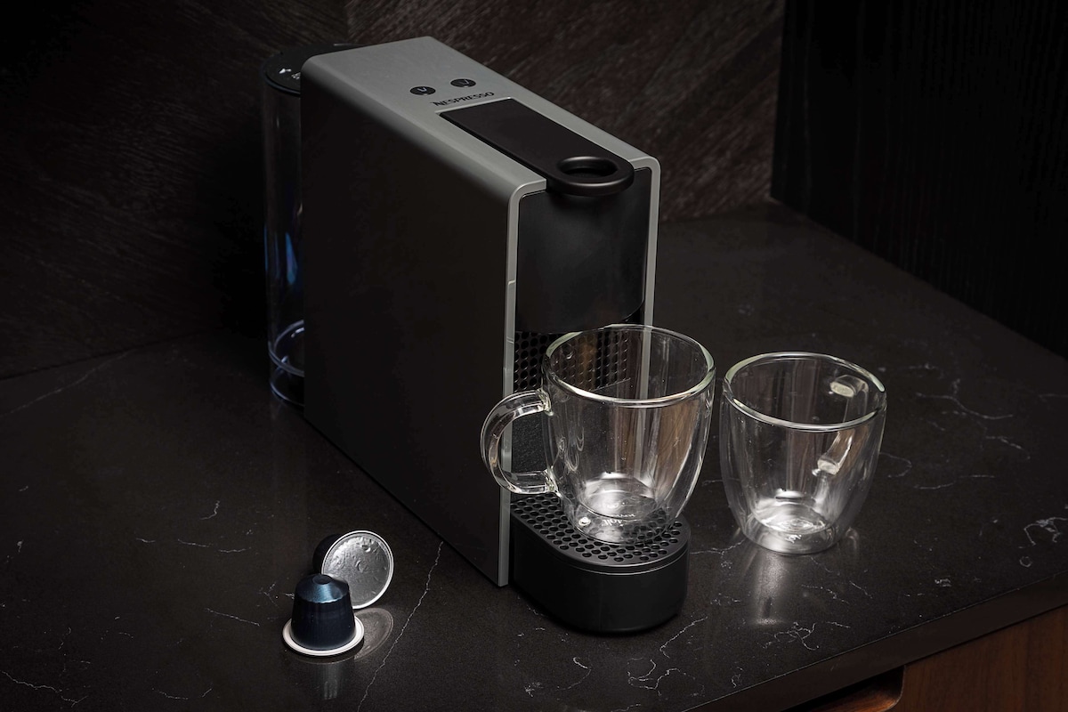 Uma cafeteira moderna com duas chávenas de vidro transparente sobre um balcão de mármore.