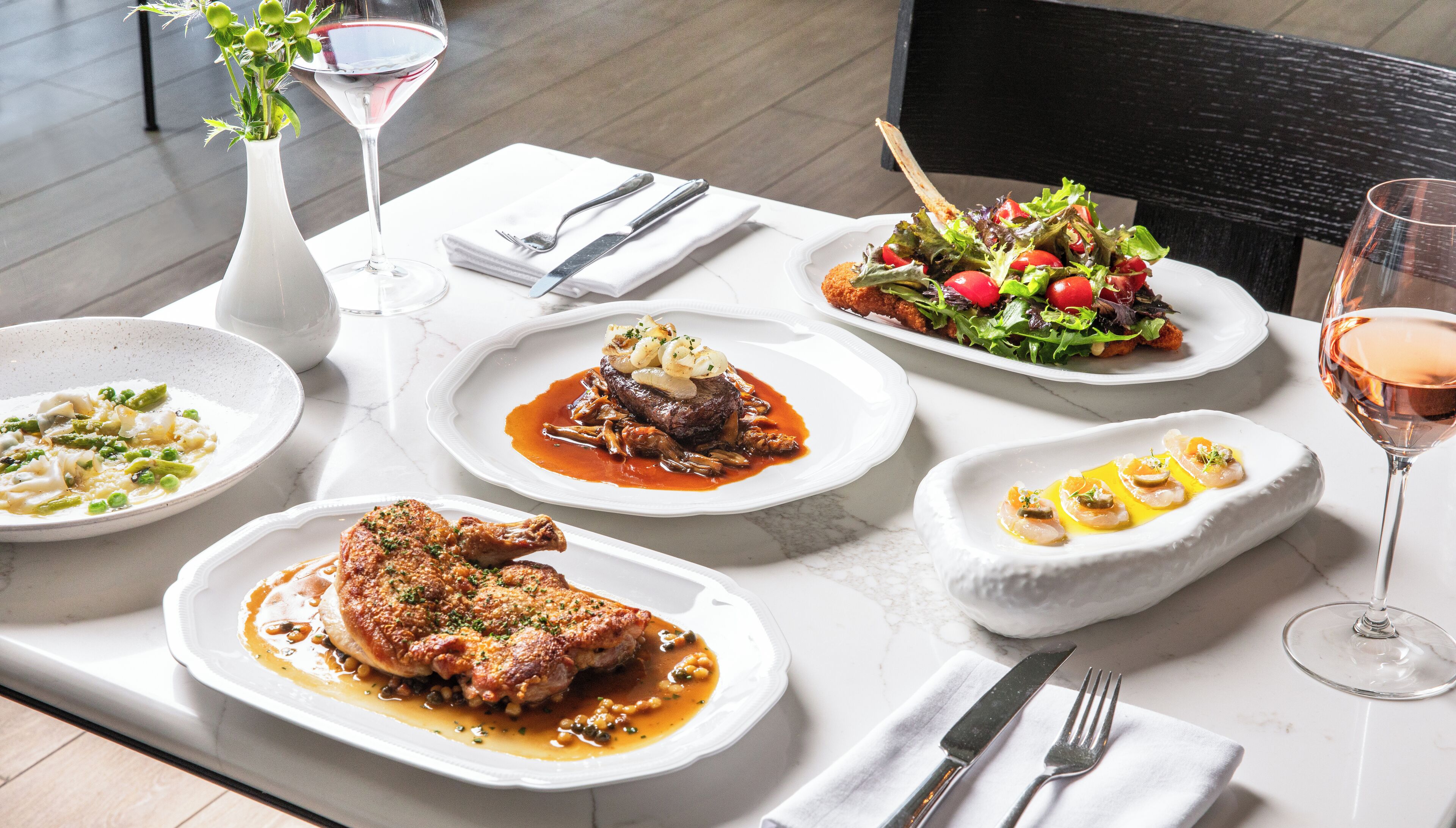 A dining table with various dishes, including a steak, salad, and seafood, along with wine glasses and cutlery.