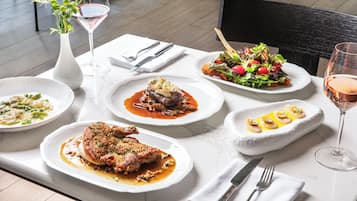 A dining table with various dishes, including a steak, salad, and seafood, along with wine glasses and cutlery.