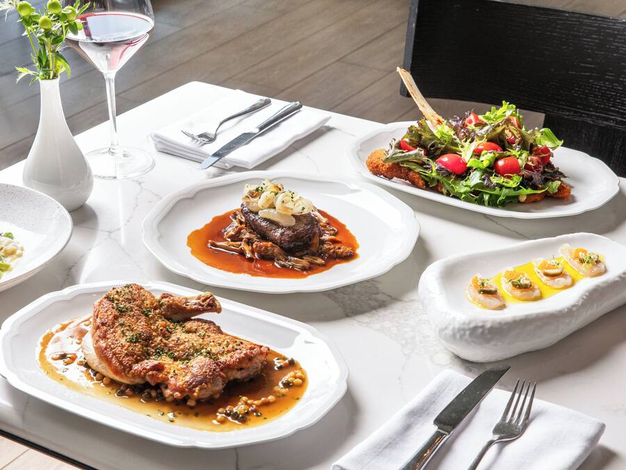 A dining table with various dishes, including a steak, salad, and seafood, along with wine glasses and cutlery.