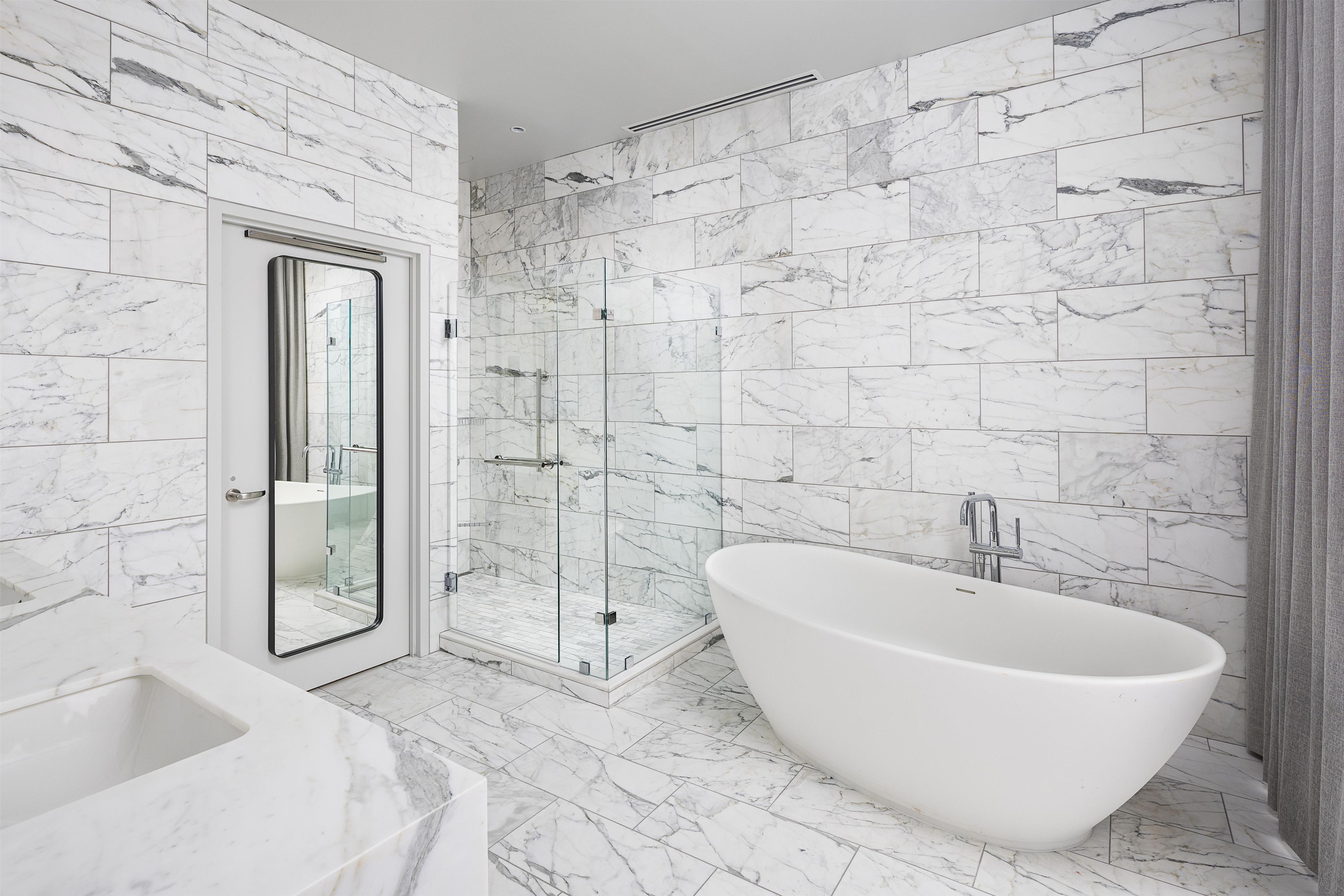A modern bathroom with a freestanding bathtub, a glass-enclosed shower, and a marble-tiled shower wall.