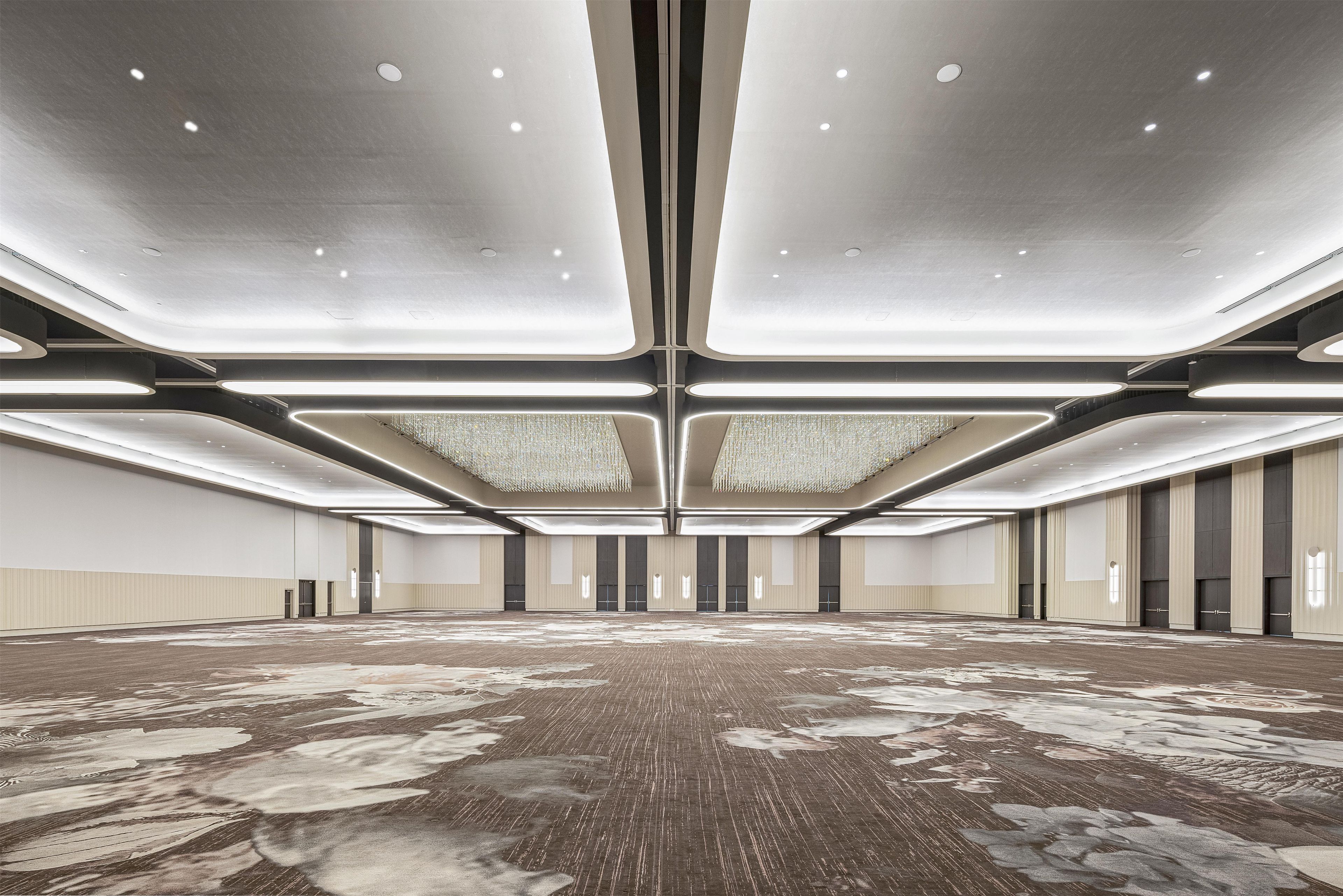 A spacious conference room with a high ceiling, recessed lighting, and a patterned carpet.
