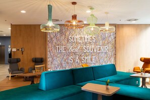 Un espacio de sala moderno con un sofá azul verdoso, mesas de madera y luces colgantes de colores.
