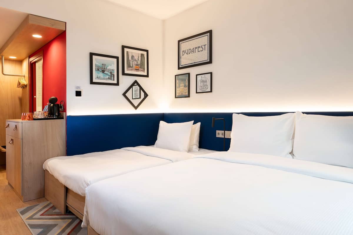 A hotel room with a large bed, a desk with a lamp, and framed pictures on the wall.