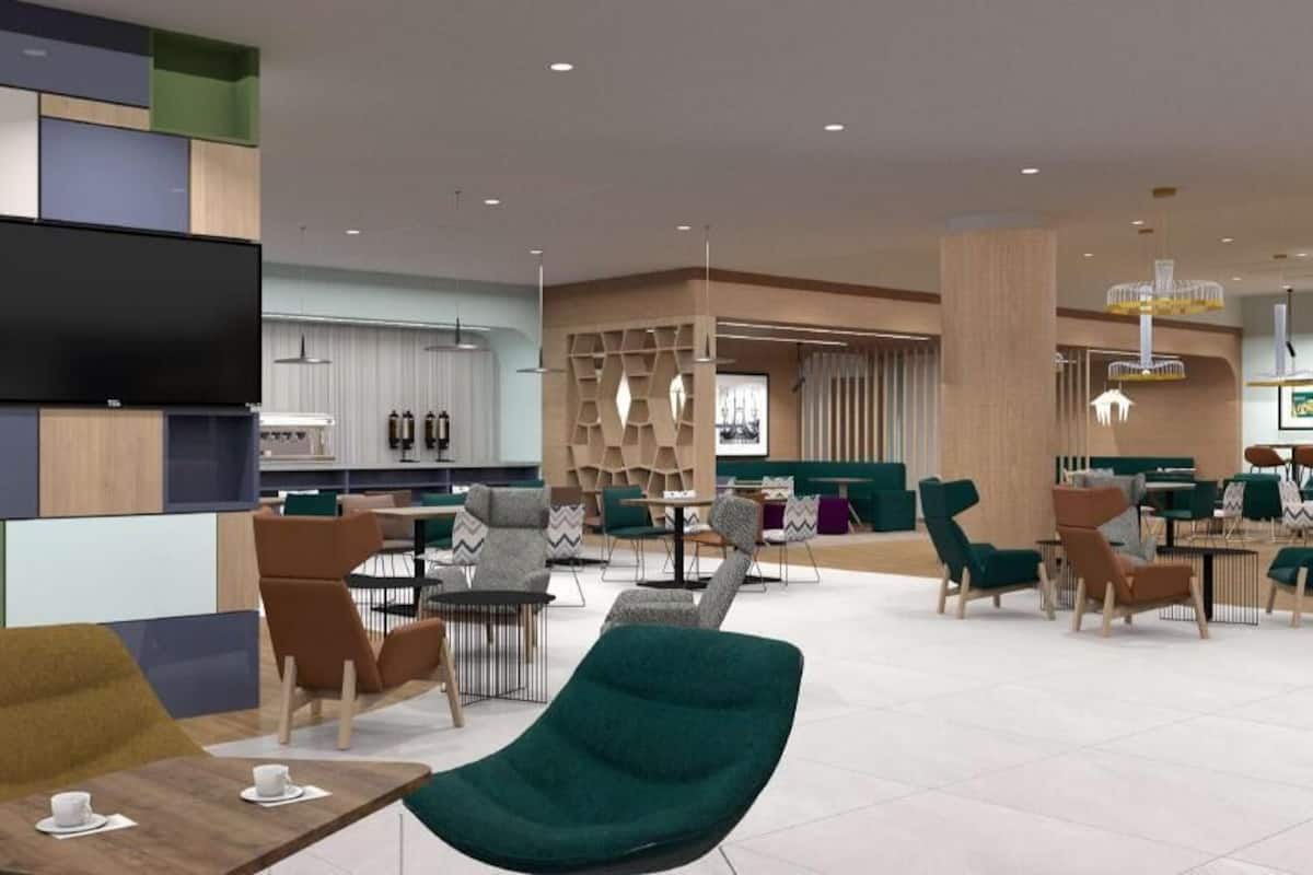 A modern hotel lobby with a TV, seating areas, and a kitchen in the background.