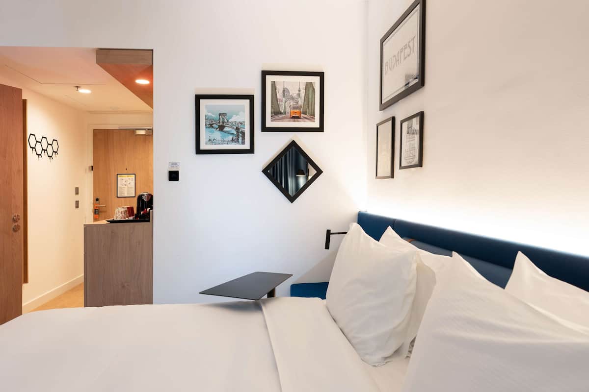 A hotel room with a bed, a desk, and a wall with framed pictures.