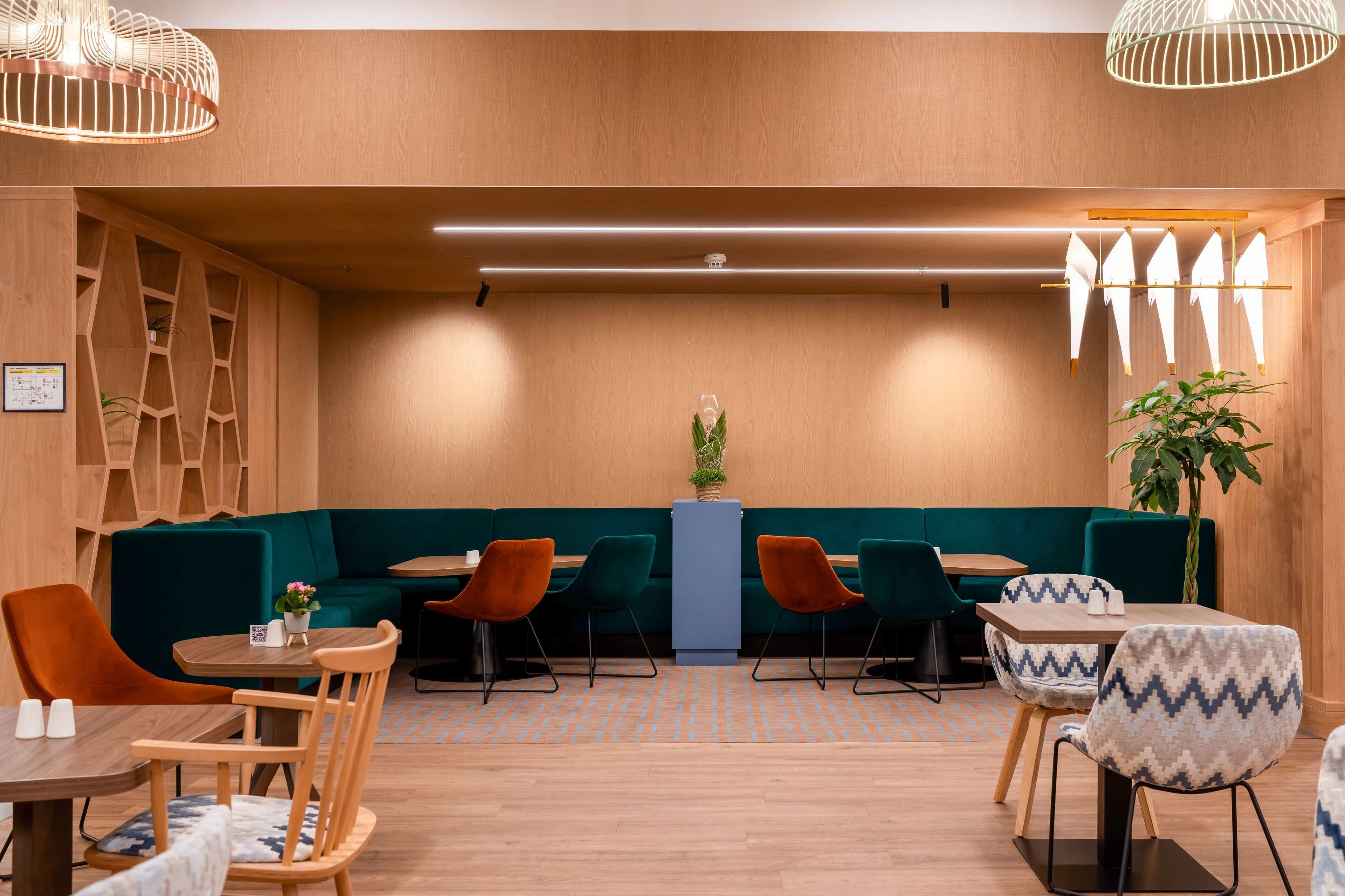 A modern restaurant with wooden walls, green seating, and pendant lighting.