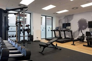 Un gimnasio con diferentes equipos de ejercicio, como mancuernas, una banca y cintas de correr.