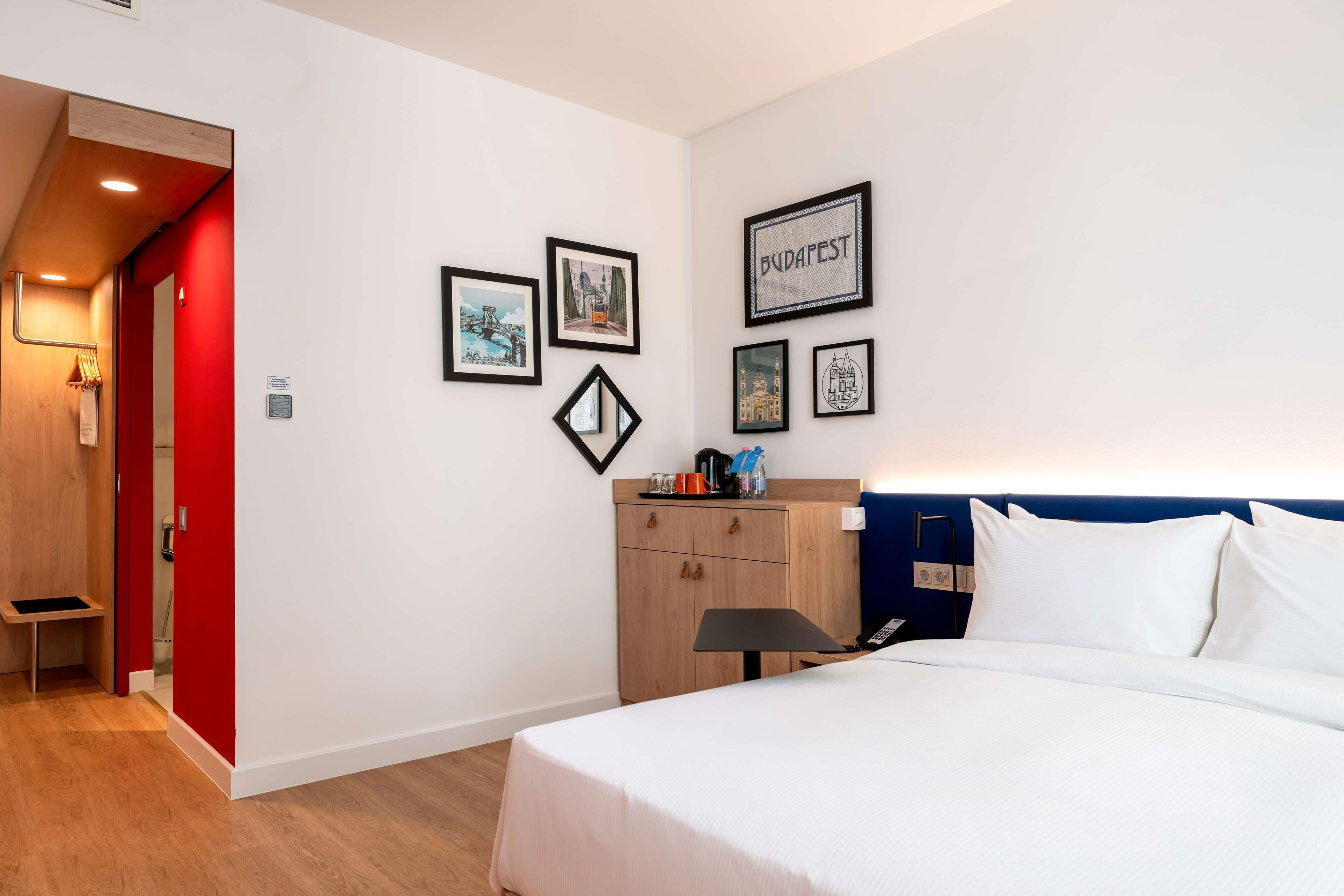 Habitación de hotel con cama, armario de madera, escritorio y una pared decorada con cuadros.