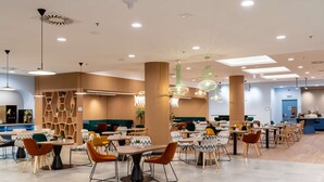Un comedor moderno con varias mesas y sillas, una columna central e iluminación colgante.