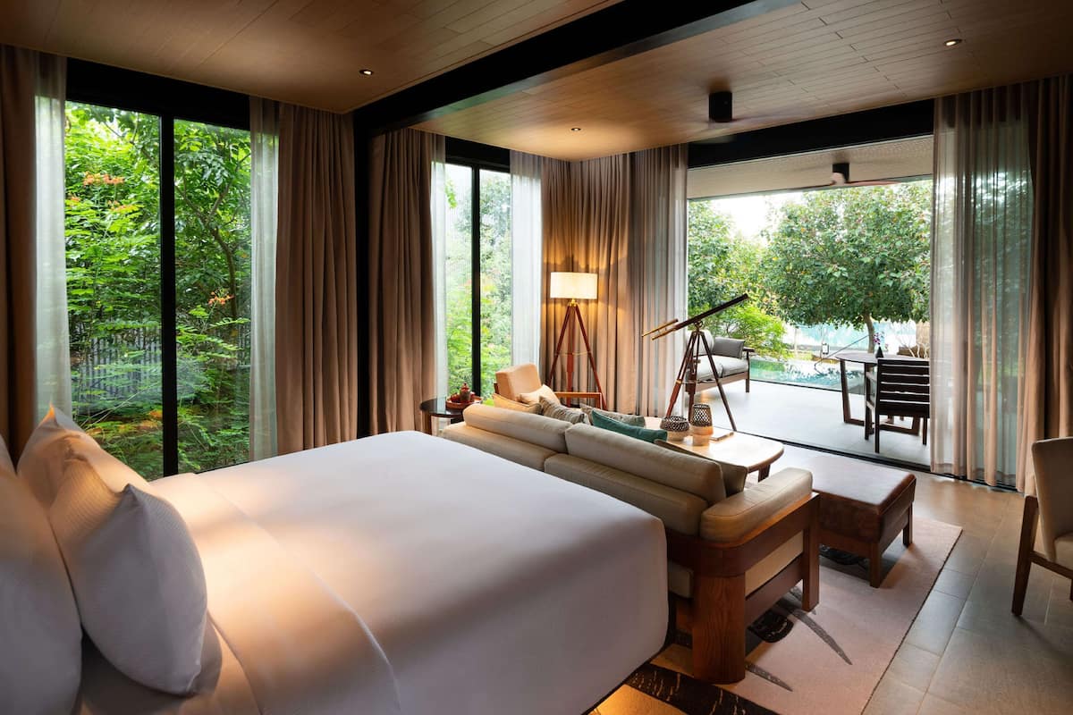 A modern hotel room with a large bed, a sofa, a desk, and a balcony with a telescope.