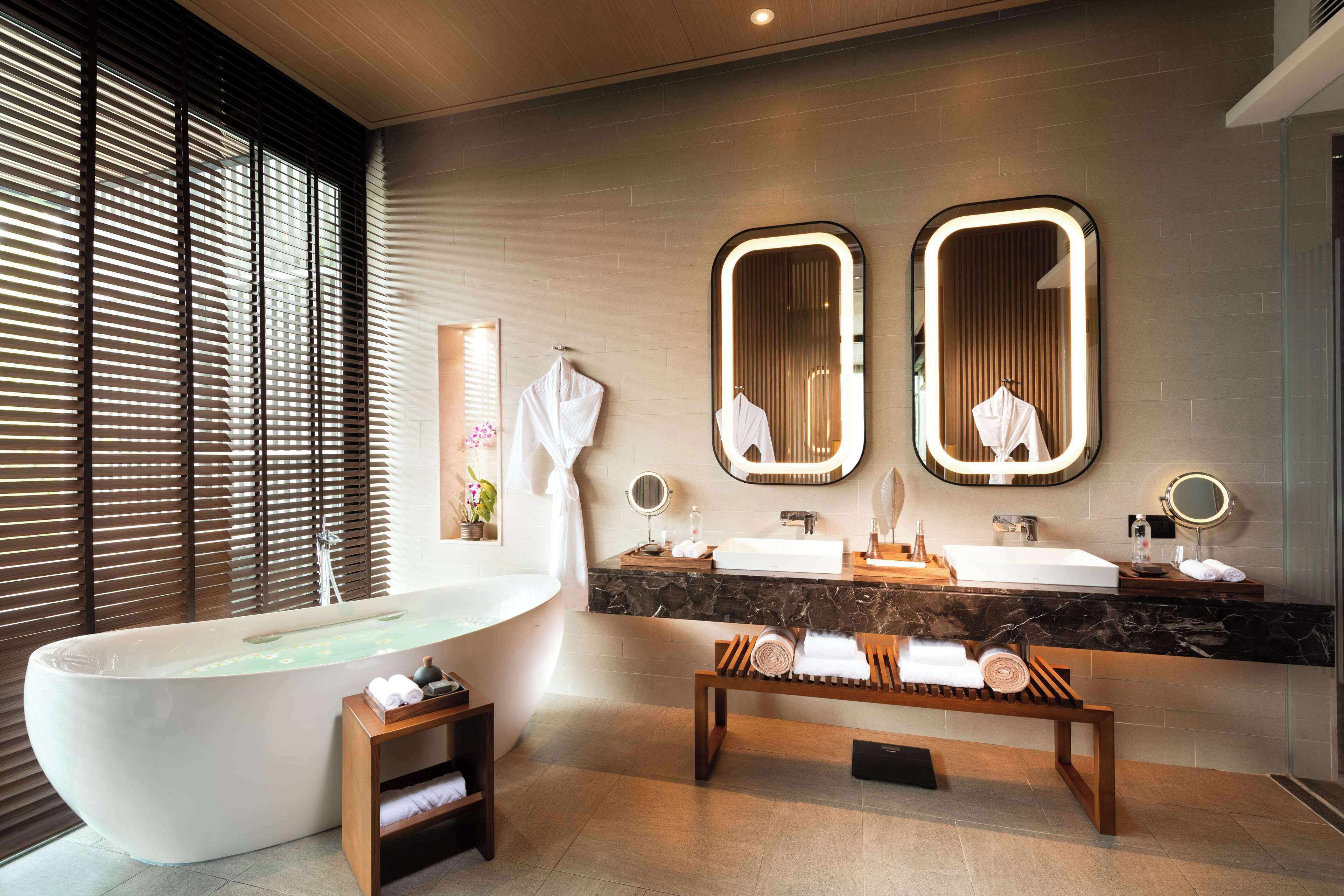A modern bathroom with a freestanding bathtub, dual vanity sinks, and a bench with towels.
