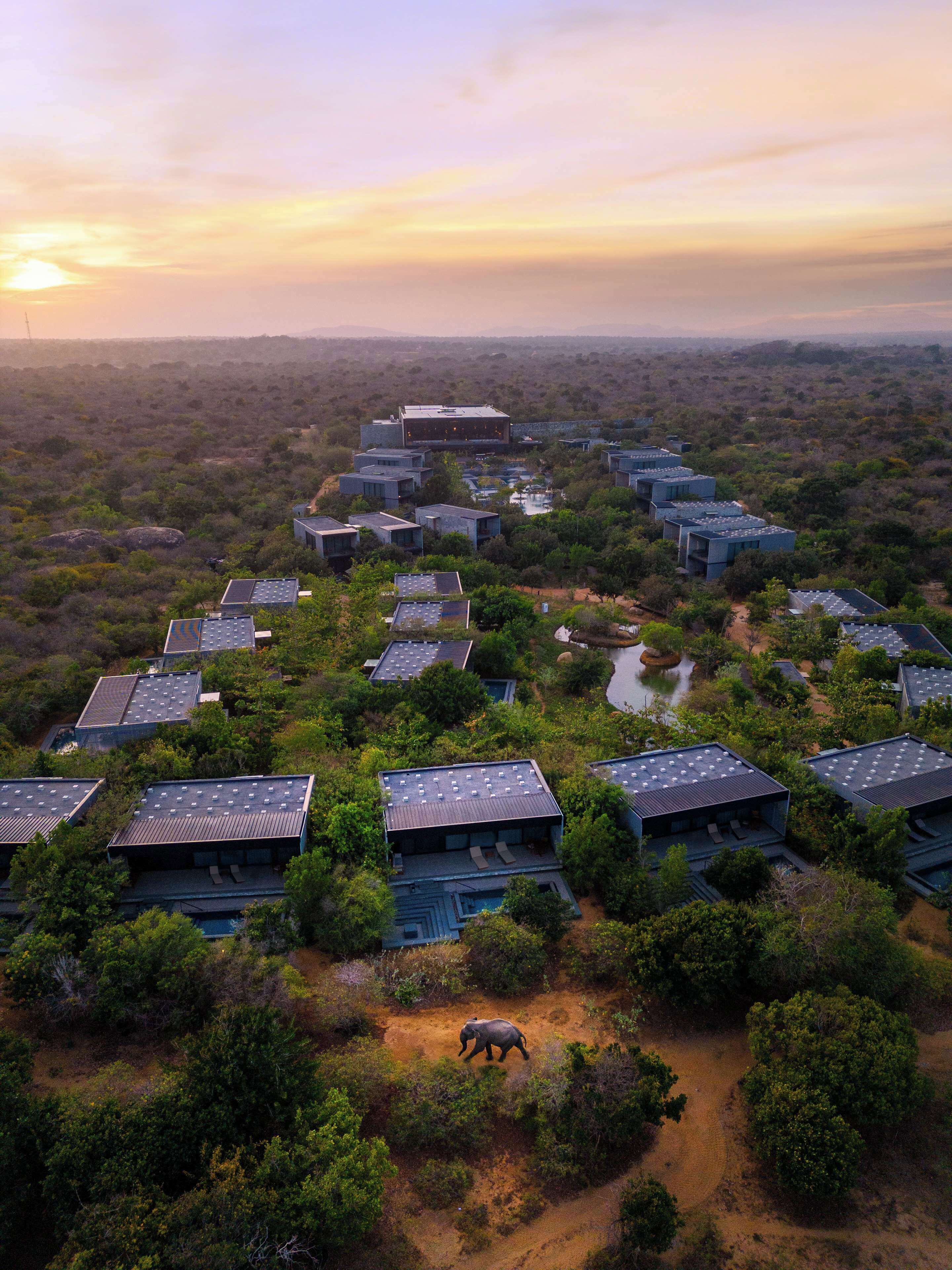 An aerial view of a resort with multiple buildings, a central water feature, and a walking path.