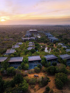 An aerial view of a resort with multiple buildings, a central water feature, and a walking path. - Hilton Yala Resort (Thissamaharama)