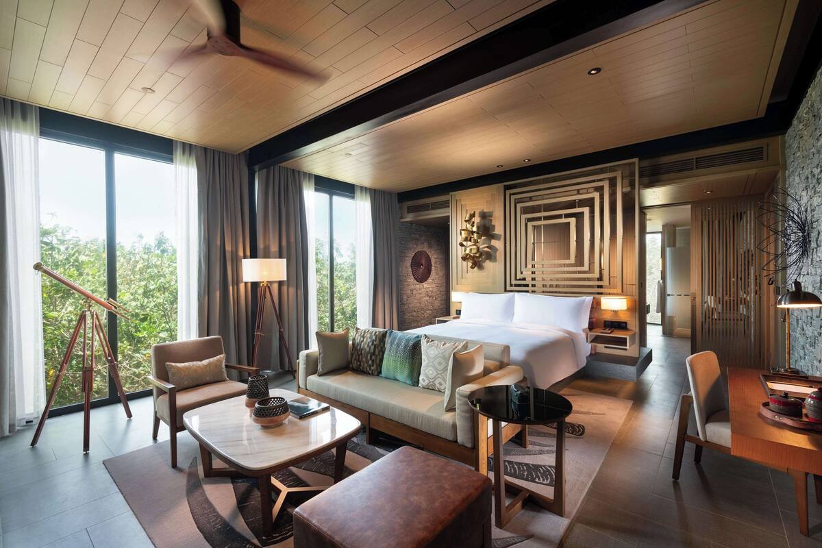 A modern hotel room with a large bed, a sofa, a dining table, and a telescope.