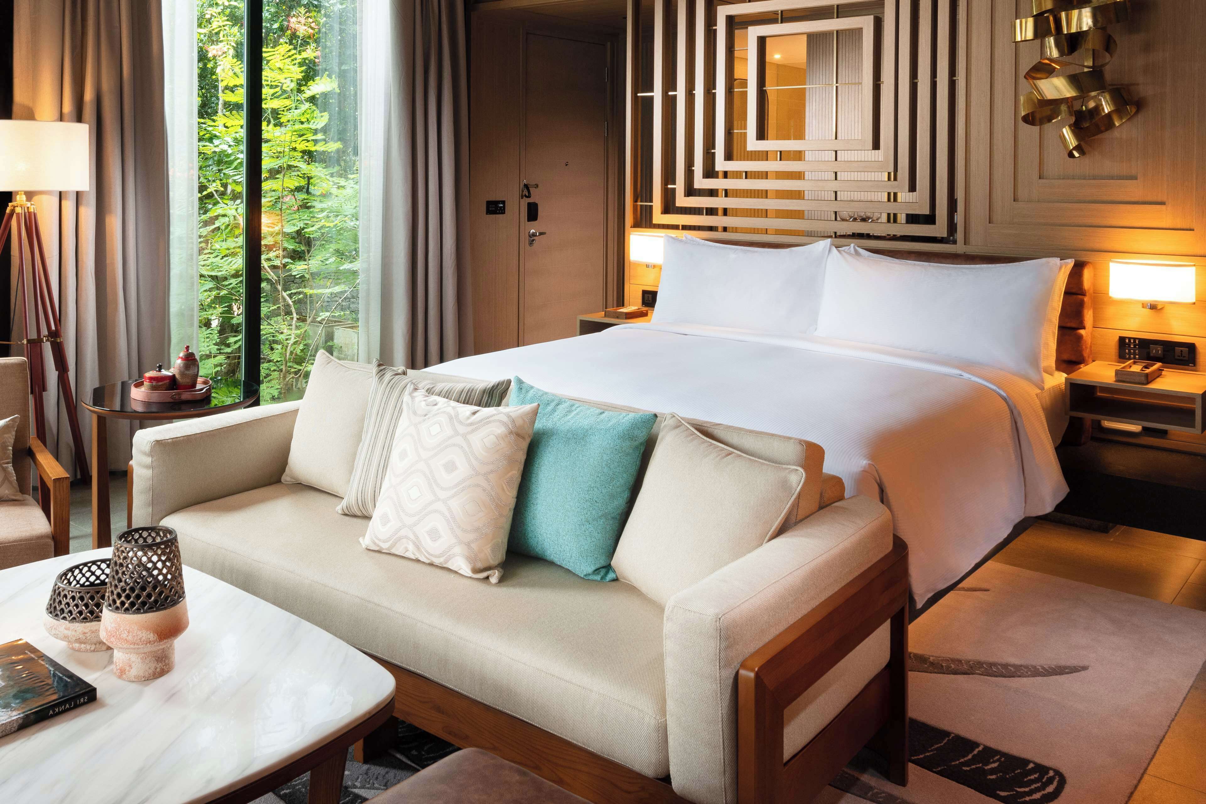 Una habitación de hotel con una cama grande, un sofá, una mesita de centro y una mesita de noche con lámpara.