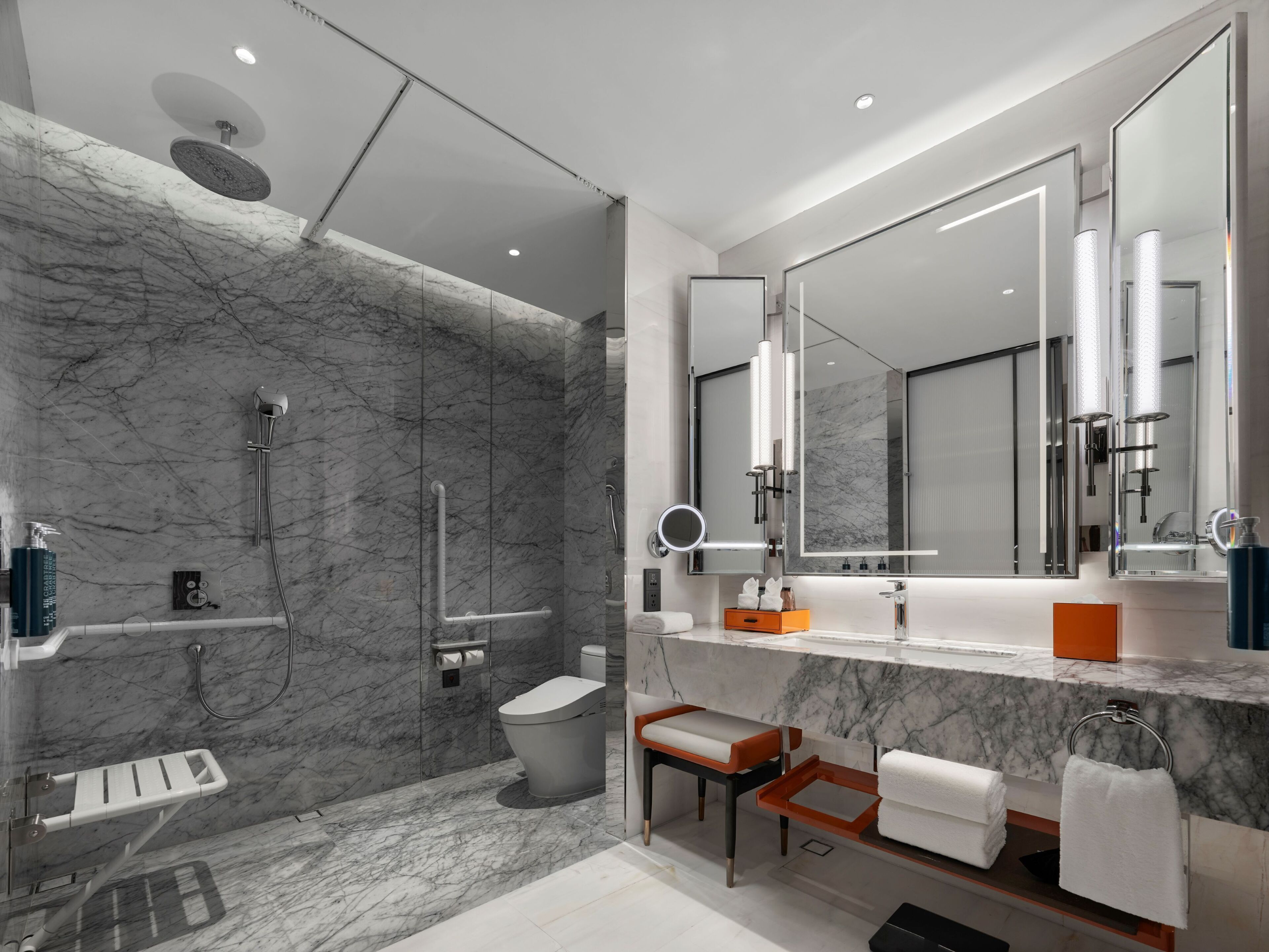 A modern bathroom with a marble wall, a shower, a toilet, a sink, and a vanity.