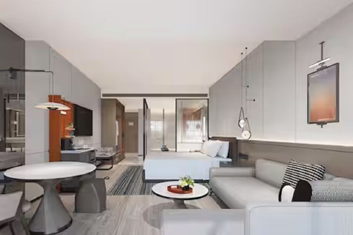 A modern hotel room with a dining area, a sofa, a bed, and a TV.