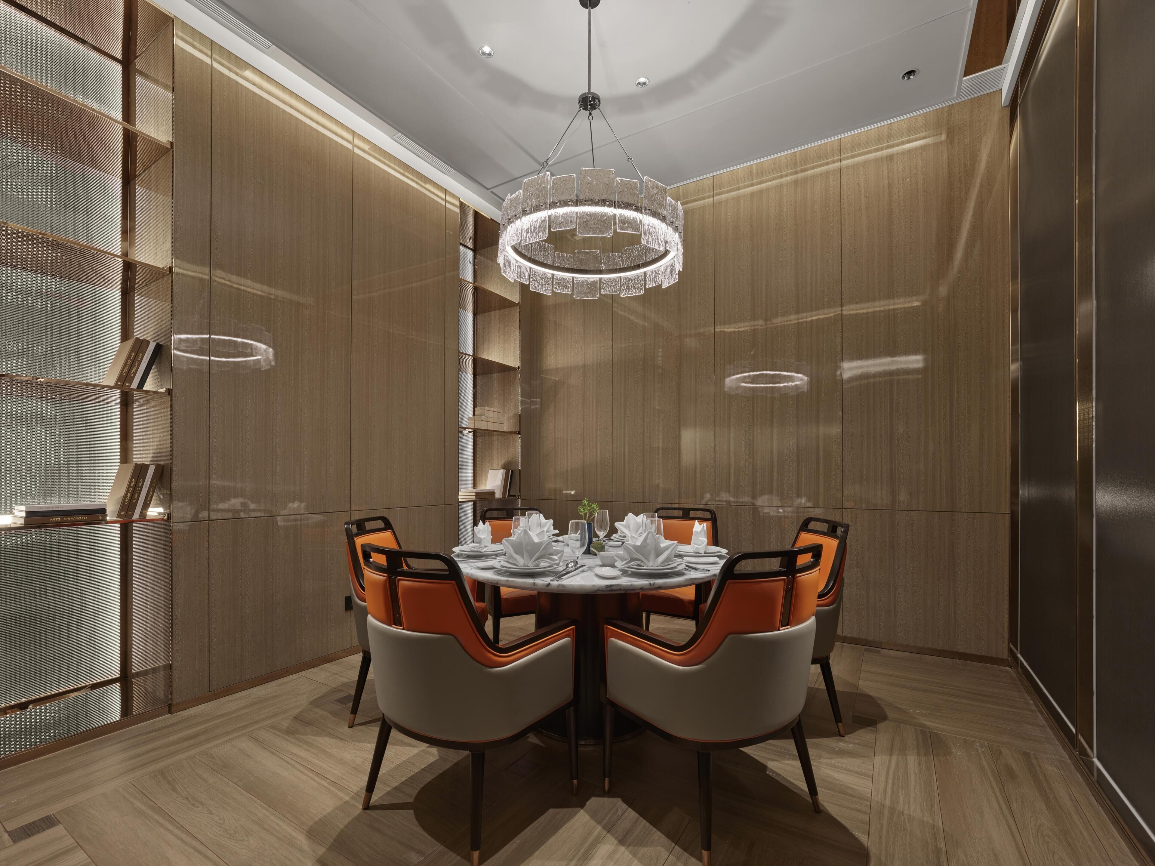 A modern dining area with a round table, orange chairs, and a chandelier.