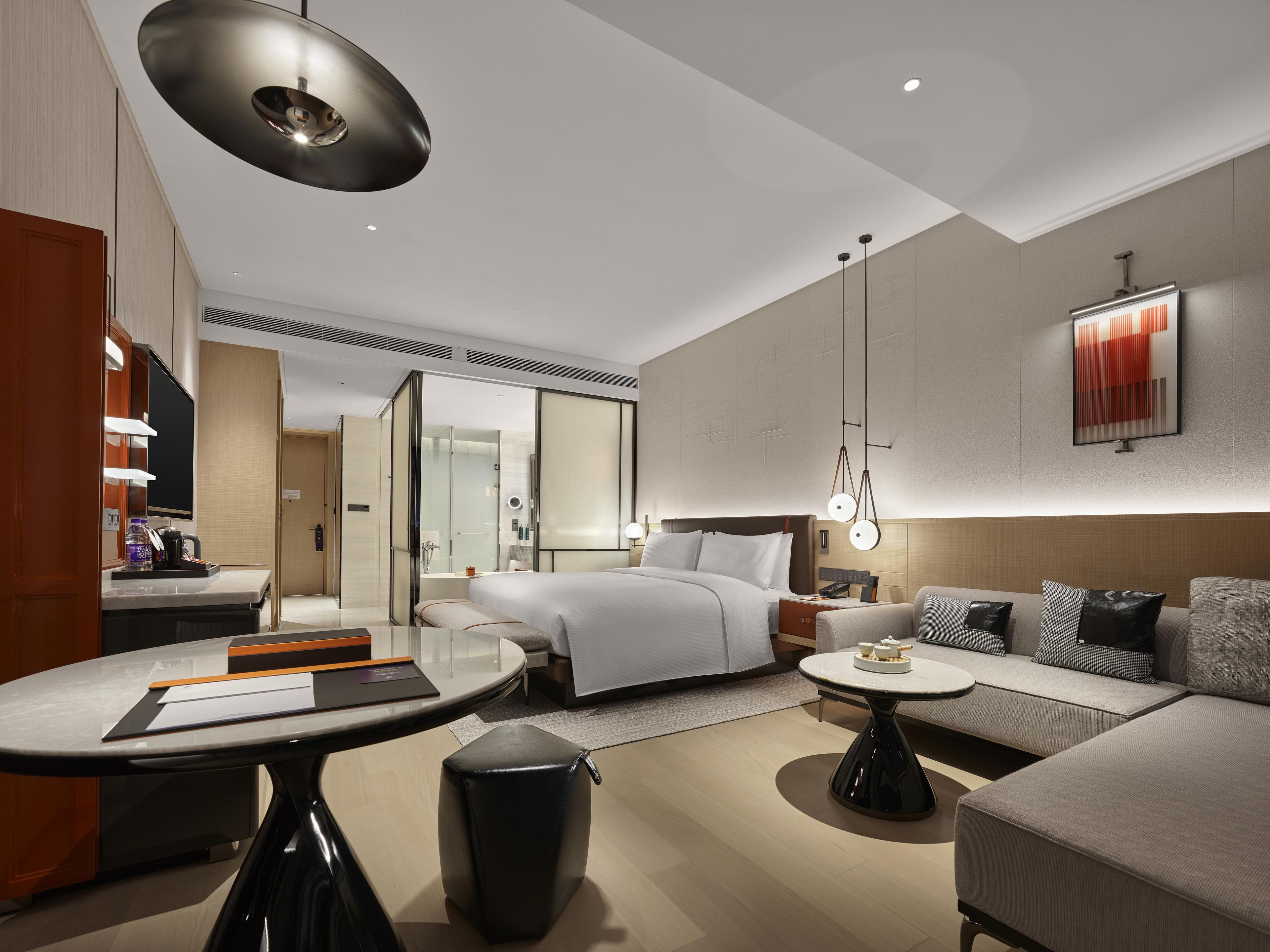 A modern hotel room with a bed, sofa, and a dining area.