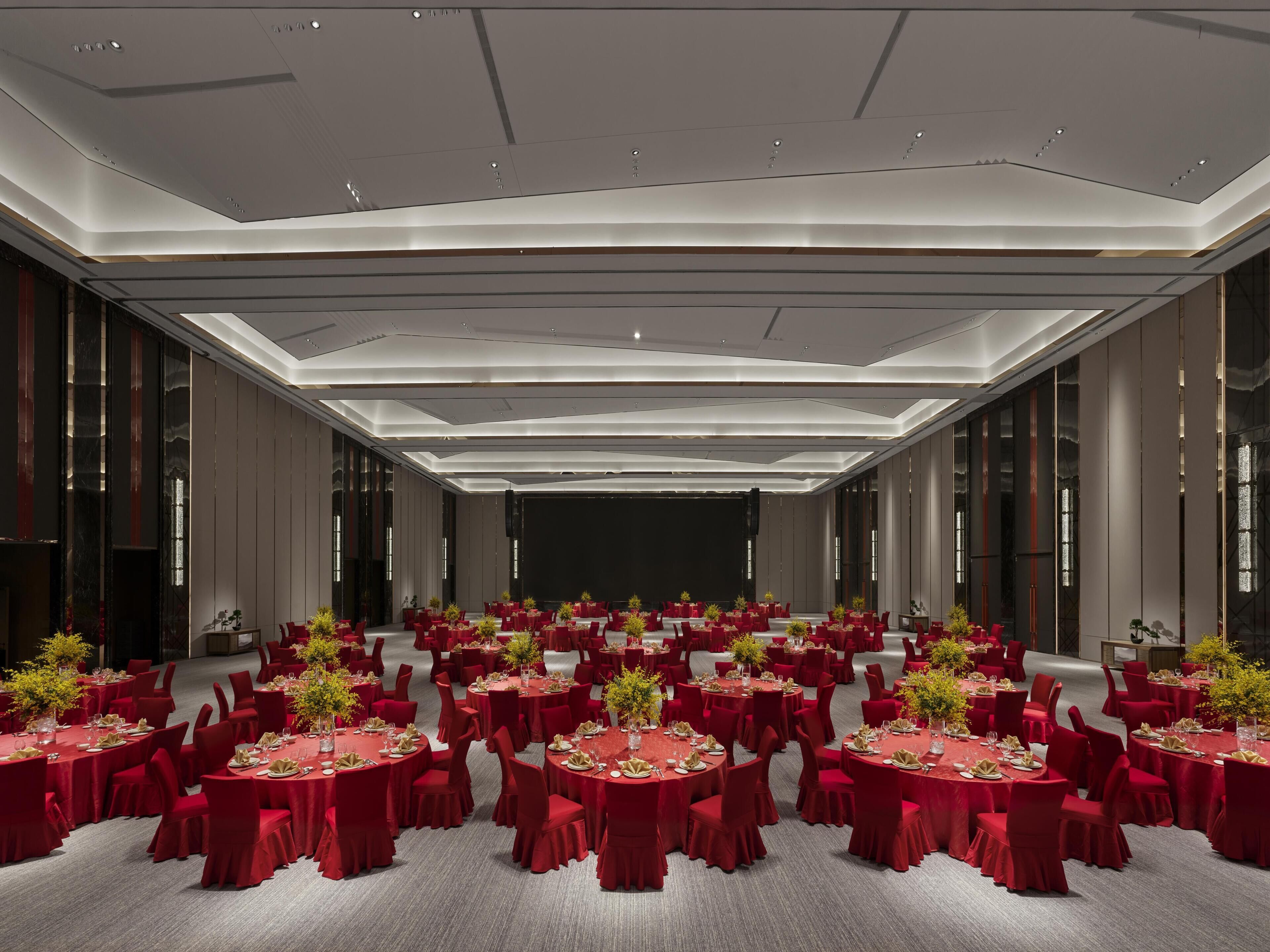 A large conference room with round tables, red chairs, and a stage.
