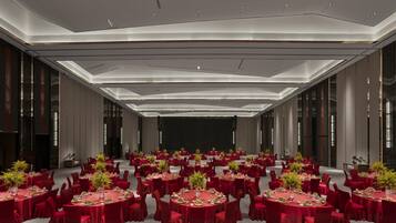 A large conference room with round tables, red chairs, and a stage.