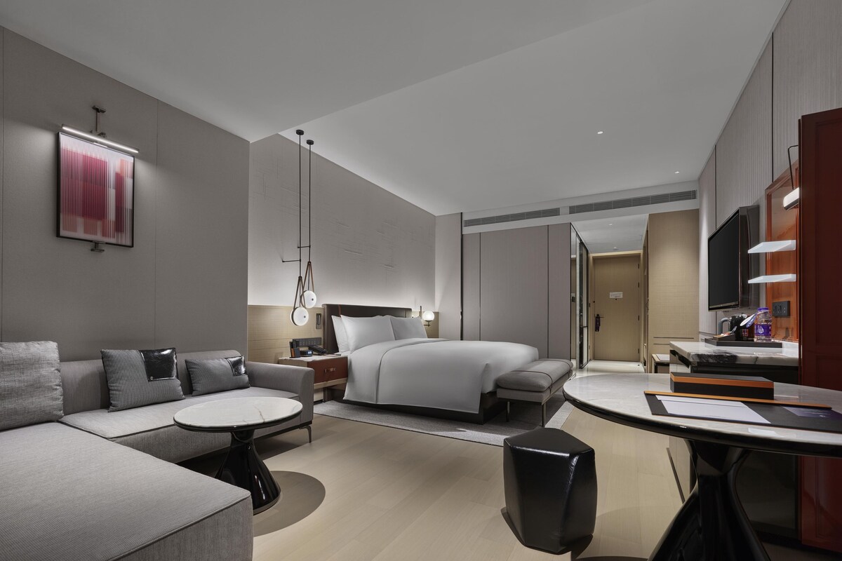 Habitación de hotel moderna con sofá, una mesa redonda, cama, televisor y baño.