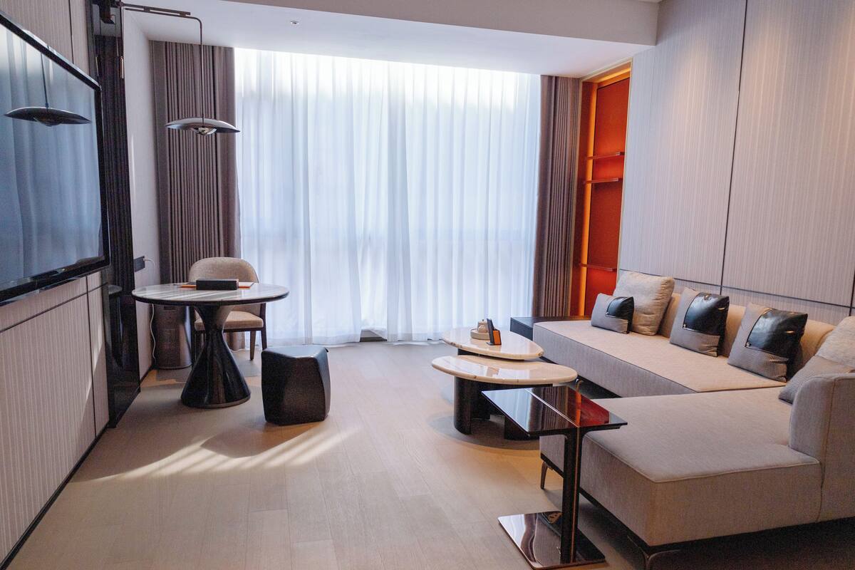 A modern hotel room with a sofa, a dining table, and a TV.