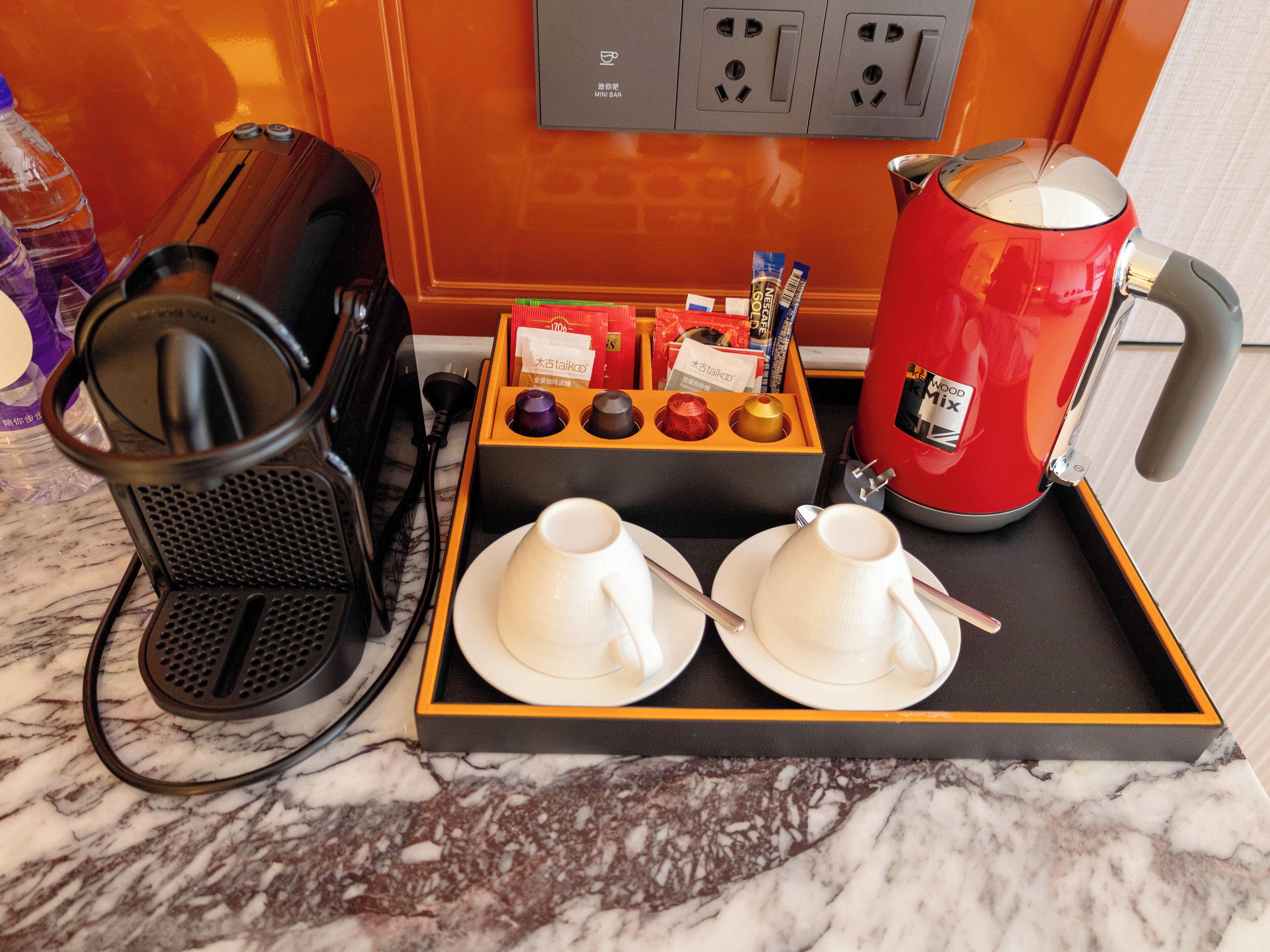 A tray with two white cups, a red kettle, a black coffee maker, and a box of tea bags.