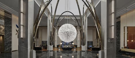 A spacious lobby with a reflective floor, a large circular chandelier, and modern furniture.