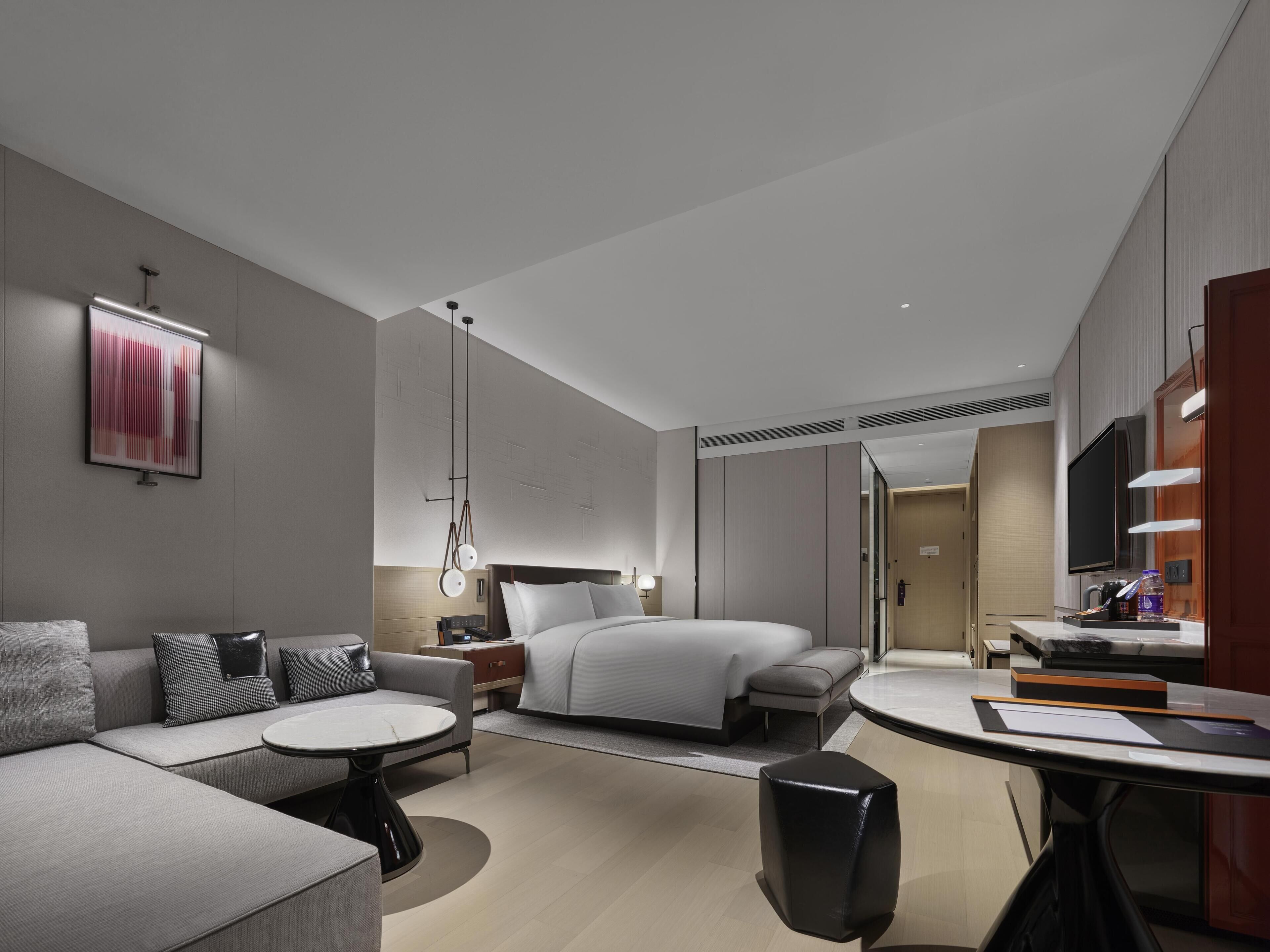 A modern hotel room with a sofa, a round table, a bed, a TV, and a bathroom.