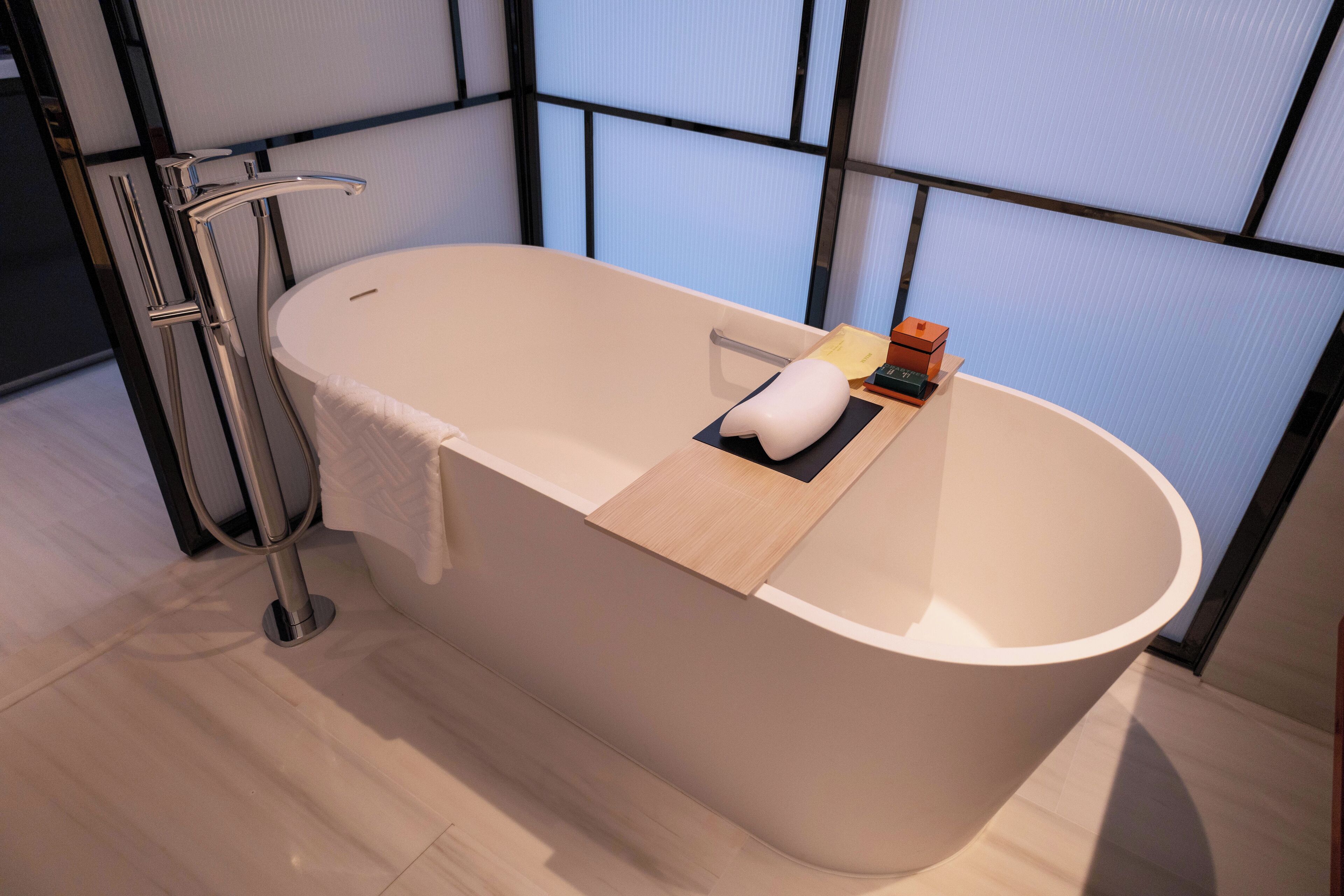 Un baño moderno con una bañera independiente, un perchero y una bandeja de madera con artículos de aseo.