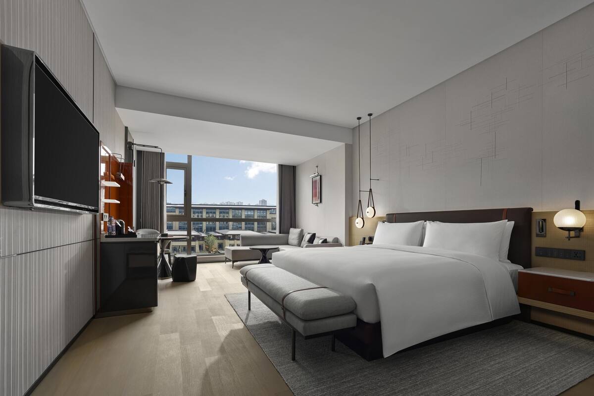 A modern hotel room with a large bed, a desk, a chair, and a TV.