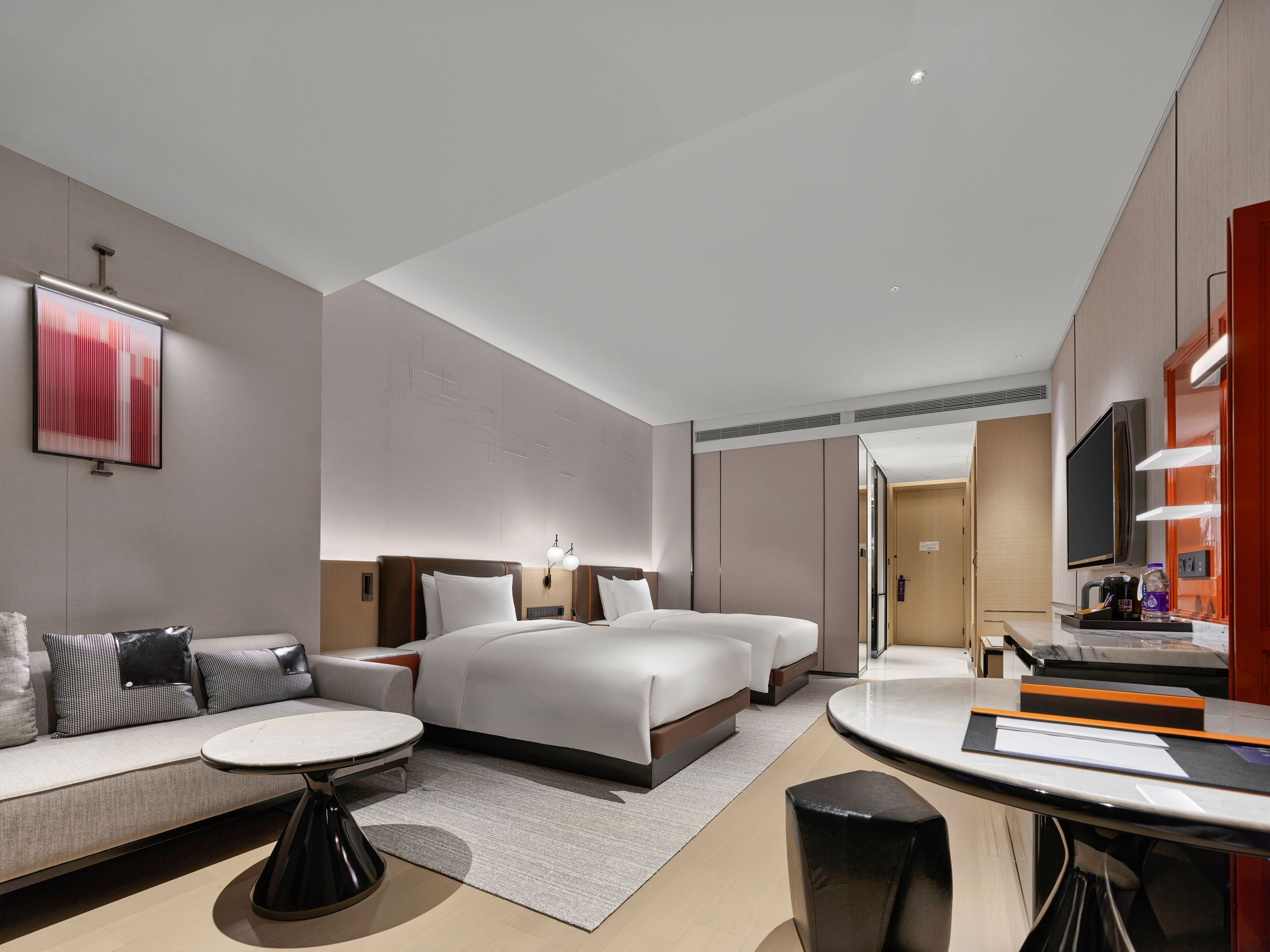 A modern hotel room with a large bed, a sofa, a dining table, and a TV.