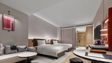 A modern hotel room with a large bed, a sofa, a dining table, and a TV.