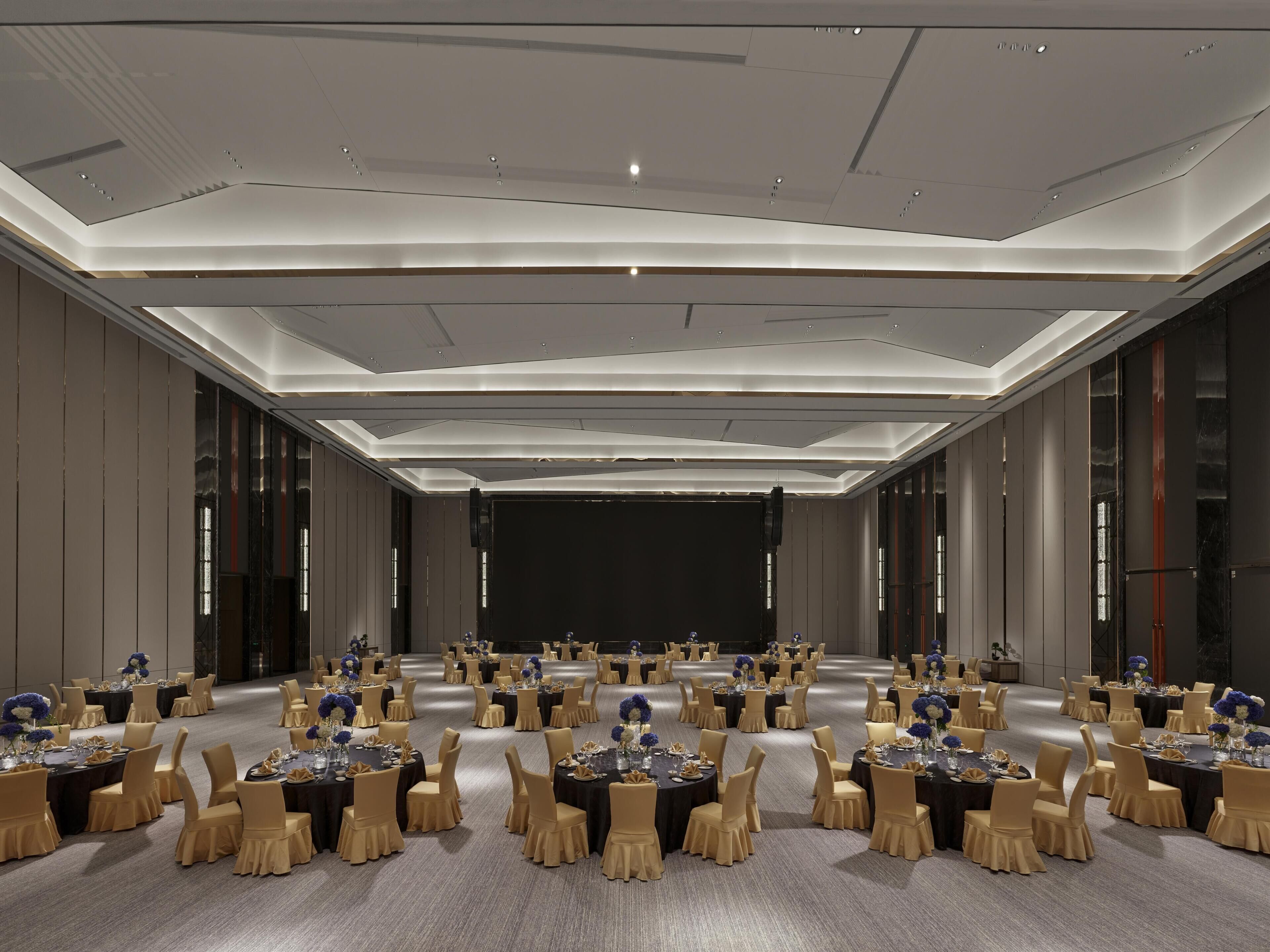 Un amplio salón de conferencias con mesas redondas, sillas y un escenario.